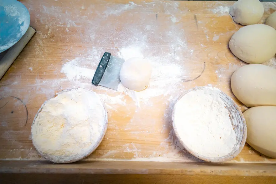 Teig, Gärkörbchen und Mehl auf dem Holztisch der Backstube